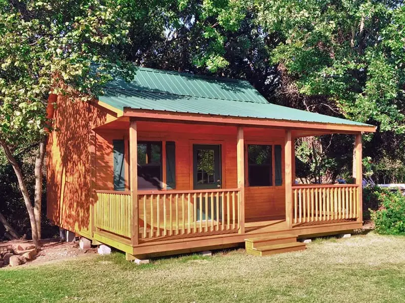 A small cabin with green roof and wooden deck.